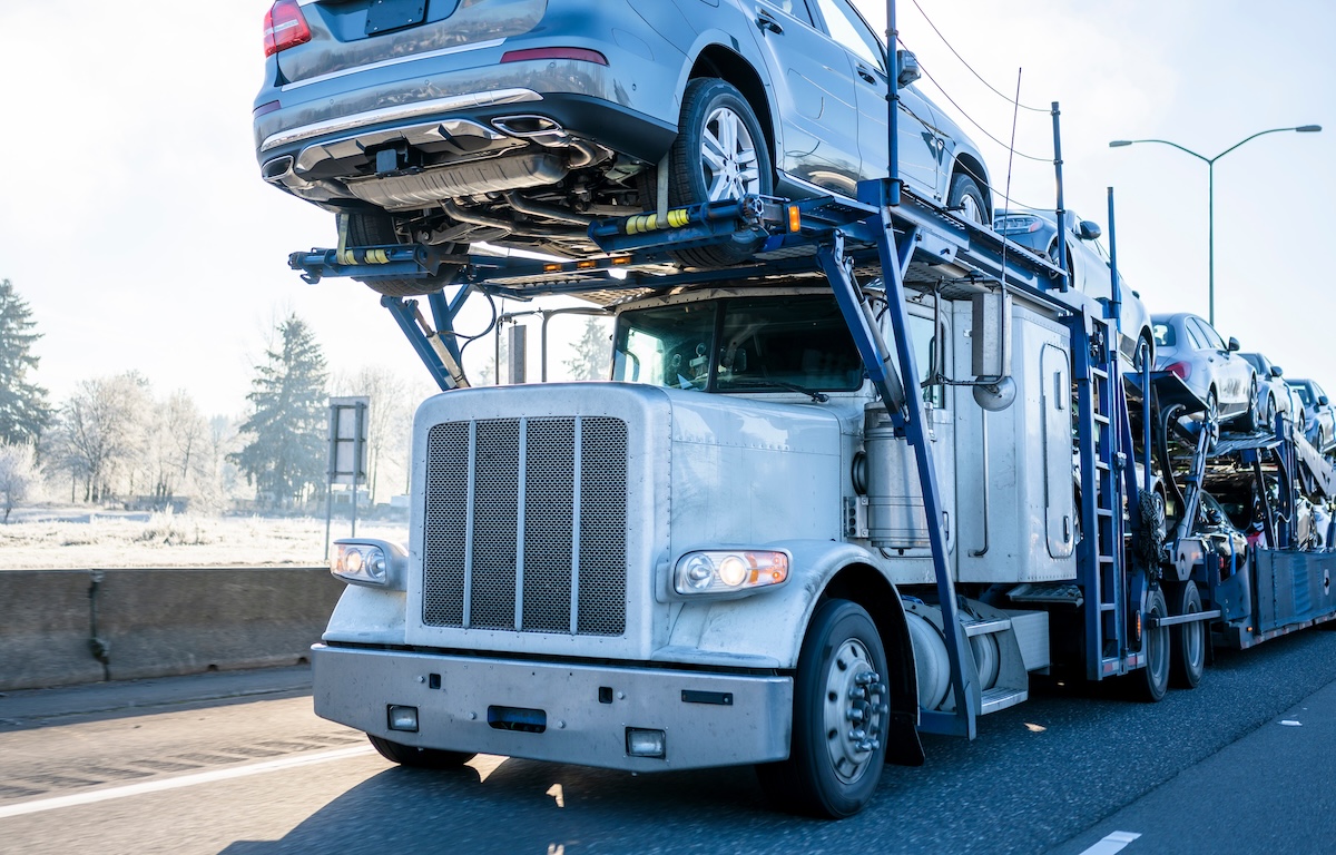 Big rig car hauler professional bonnet powerful semi truck transporting cars on two levels industrial semi trailer driving on winter frosty road with frost grass and trees on roadside
